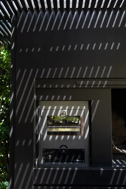 Área de parrilla moderna con pergola y sombras lineales — proyecto Quincho SA, por Estudio Junor, en Pilar